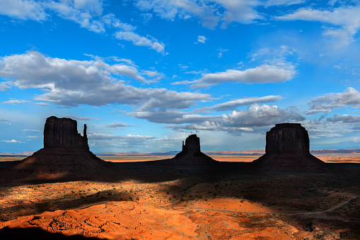 Dramatic and scenic view of the magnificent butte & mittens in shadow at Monument Valley Arizona during a partly cloudy day