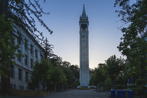 The Sather Tower emerges from the stillness of dawn, its silhouette contrasting with the scattered tents of a protest camp.