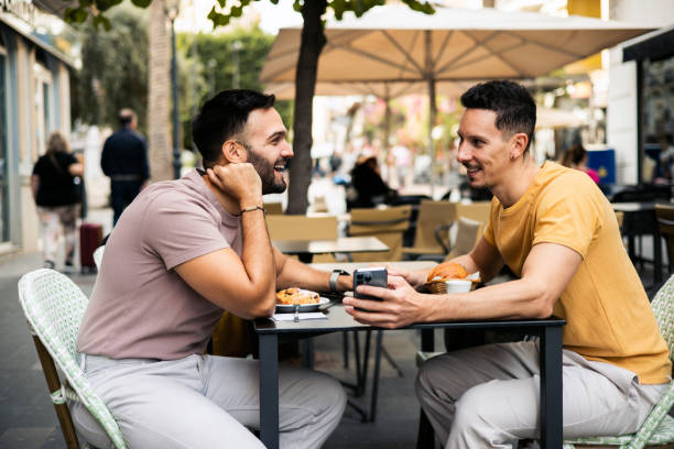 istock Gay couple enjoying breakfast and using smartphone at the cafe 2151624688