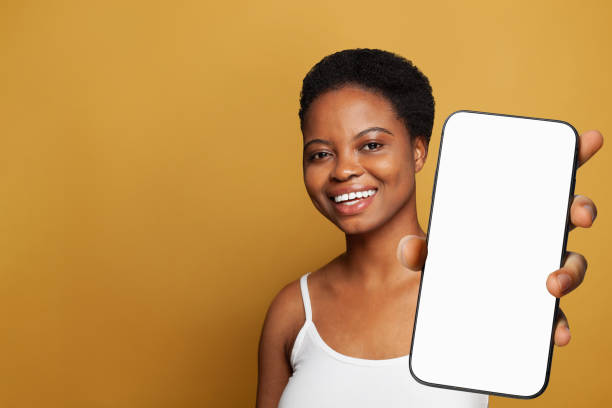 istock Brunette healthy woman holding smartphone with white empty blank screen display on yellow studio wall background. Happy model with phone 2151625062