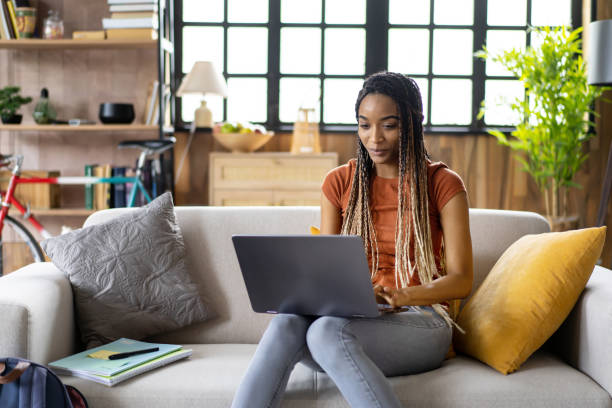 A millennial girl is learning sitting on sofa at home