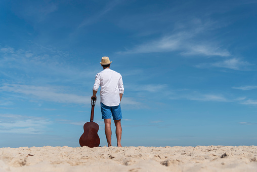 Young men playing acoustic guitar on the beach. Happy man person playing acoustic guitar music instrument seaside sitting on sand tropical beach island. Asian musician Happy guitarist hobby lifestyle