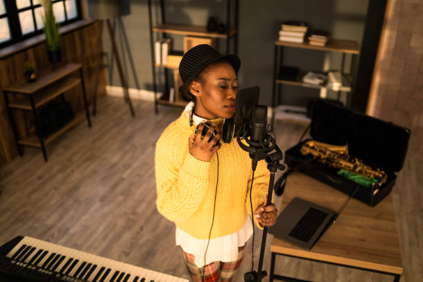 A brightly dressed female vocalist is standing and holding the microphone stand while rehearsing and recording her songs in a sound recording studio