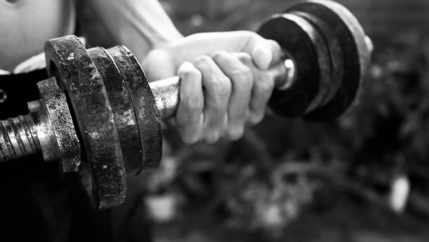 Person lifting weights with dumbbell in hand in black and white background.