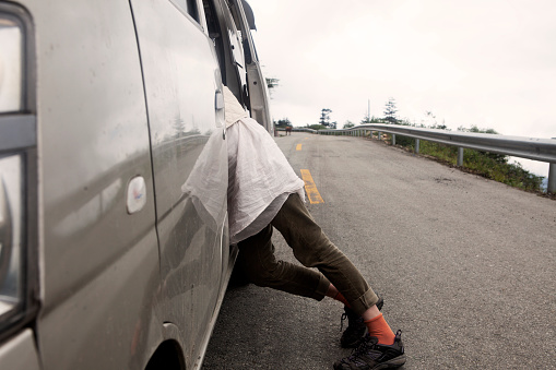 A view of a girls legs and orange socks as she leans into a van that is parked by the side of a mountain road