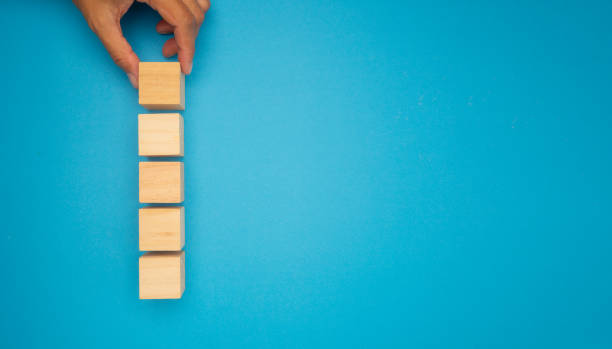 istock A hand is arranging wooden blocks in a vertical line on a vibrant blue background. 2151644838