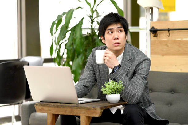 istock Young Asian man working on laptop while having a drink indoors 2151648580