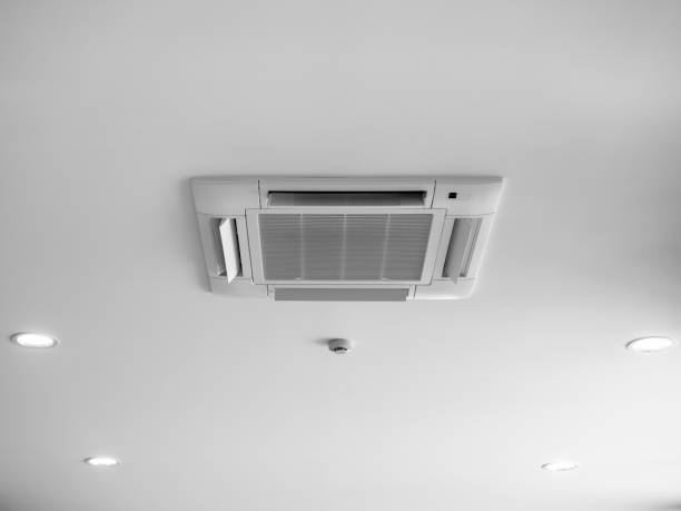 istock Ceiling mounted cassette type air conditioner decoration near ceiling lights on white building interior. Ceiling type of air conditioning unit with ventilation system. 2151651469