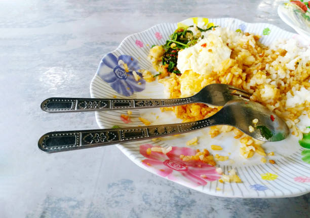 Leftover minced pork, chicken or beef and basil rice with stainless steel spoon and fork on white dish after eating done. Spicy Thai food on plate at local food street market. Remain meal.