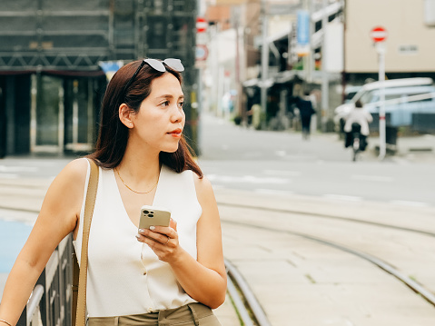 A young woman standing still on a city street, engrossed in her phone. The cool tones and blurred urban backdrop evoke a sense of serenity, reflecting her calm mood and focused emotion.