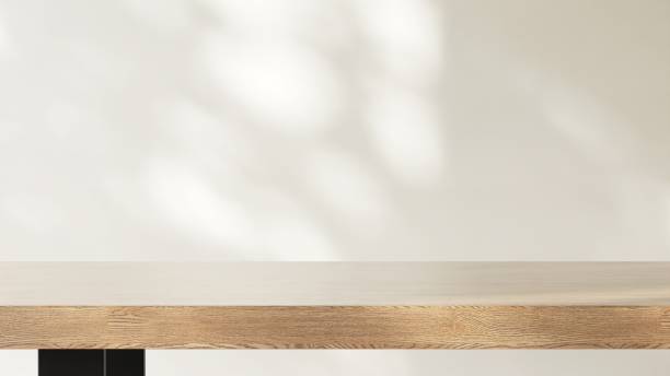 istock Minimal wooden counter table in dappled sunlight, leaf shadow on beige cream wall 2151655950