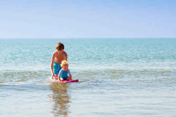 Kids playing on tropical beach. Water splash fun. Little boy splashing in sea waves. Children swim and play on summer family vacation. Sand and water toy, sun protection for young child.