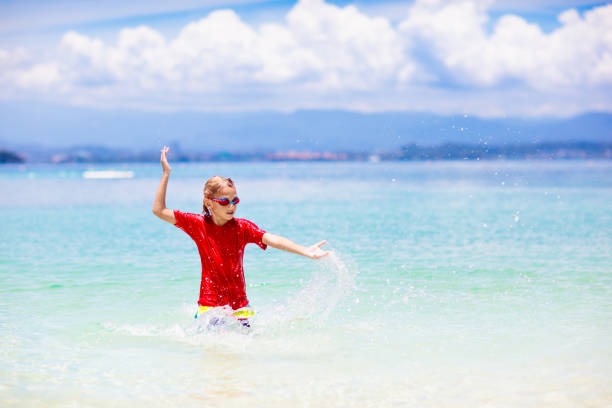 Kids playing on tropical beach. Water splash fun. Little boy splashing in sea waves. Children swim and play on summer family vacation. Sand and water toy, sun protection for young child.