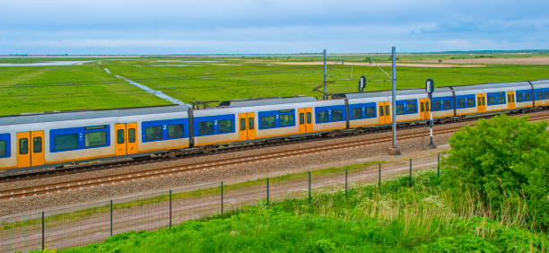 Train riding on a railroad track in wetland below a blue cloudy sky in springtime, Almere, Flevoland, The Netherlands, May 4, 2024