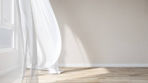 istock Empty room with cream wallpaper wall, blowing white sheer curtain in sunlight from window, tree shadow on parquet floor 2151663357