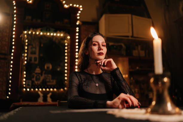istock Mysterious prophet dealing Tarot cards forecasting future for client by light of burning candles. Enigmatic wizard having divination session with tarot cards at dark esoteric room 2151666294