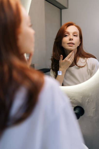istock Vertical shot of charming young redhead woman enjoying her appearance while getting ready in bathroom. Happy beautiful female touching face look in bathroom mirror 2151666905