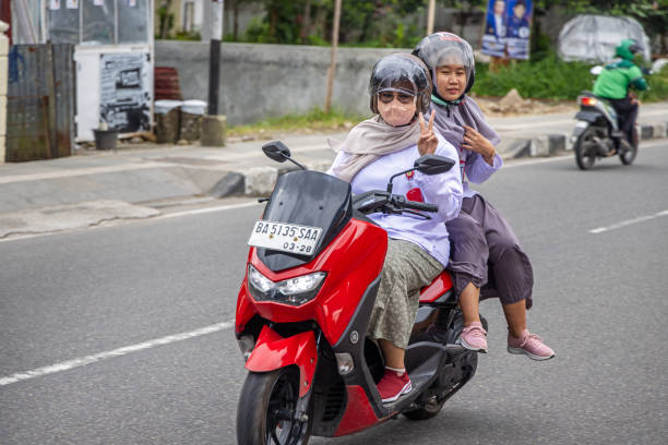 Bukittinggi, West Sumatra, Indonesia - February 5th 2024:  Two mature women with crash helmets on a motorcycle