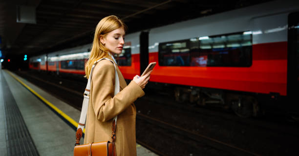 istock Female standing at subway platform with mobile phone, using social media and waiting train 2151670867