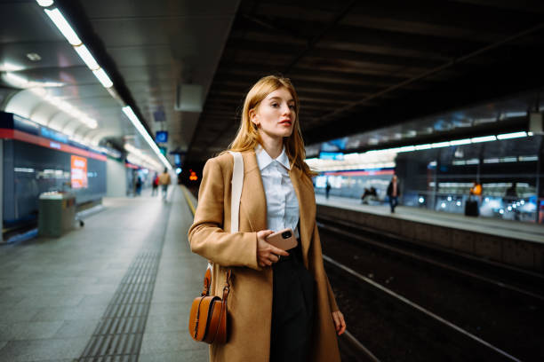 istock Female standing at subway platform with mobile phone, using social media and waiting train 2151671439