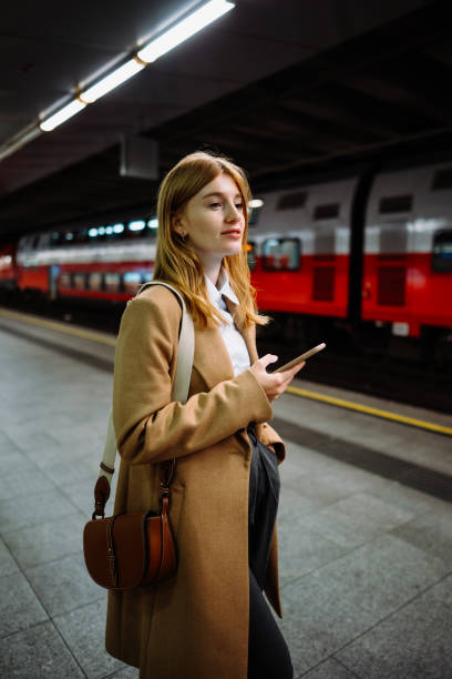 istock Female standing at subway platform with mobile phone, using social media and waiting train 2151671603