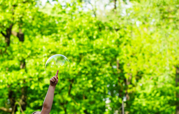 istock child trying to burst flying soap bubbles, festive atmosphere, sun rays, greenery, fun 2151673344