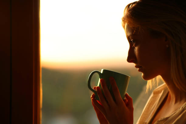istock Melancholic woman drinking coffee looking through a window 2151674443
