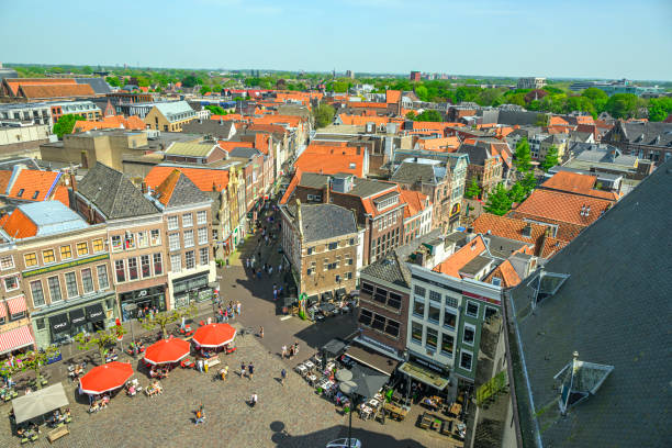 Grote Markt town square in Zwolle seen from above with shops, restaurants and bars. People are walking in the street along the shop windows and are enjoying the weather on a sidewalk cafe.