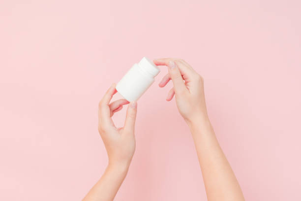 istock View on white bottle plastic tube in hands on pink background. Packaging for pills, capsules, supplements or ointment. Cosmetics 2151674956