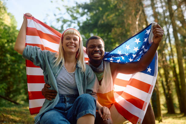 istock Cheerful multiracial couple with US flag in nature looking at camera. 2151677944