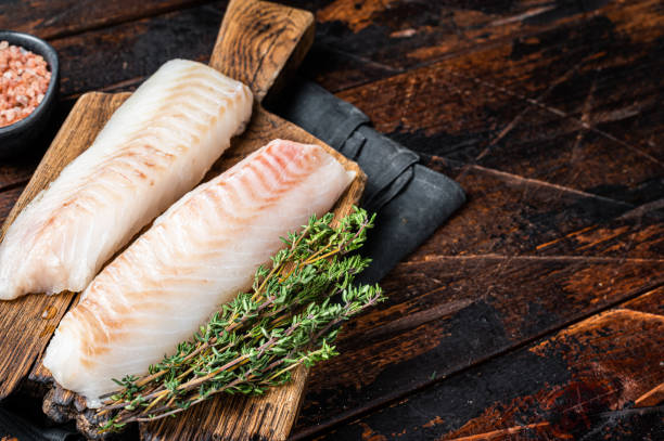 istock Cod fish fillets, raw codfish with thyme on wooden board. Wooden background. Top view. Copy space 2151678525