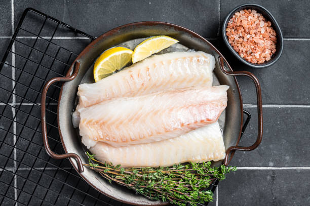 istock Fresh raw cod fish fillets with herbs served on steel tray. Black background. Top view 2151678529