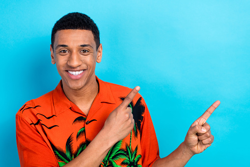 Photo of cheerful cool guy dressed print shirt showing two fingers empty space isolated blue color background.