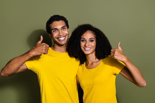 Photo of two young people show thumb up wear t-shirt isolated on khaki color background.