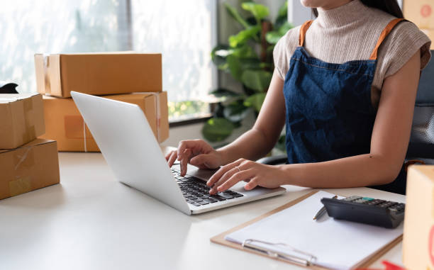 istock business operator Sell ​​products online, check customer information and orders that need to be shipped via laptop, and prepare cardboard boxes to put products in the home office. 2151691599