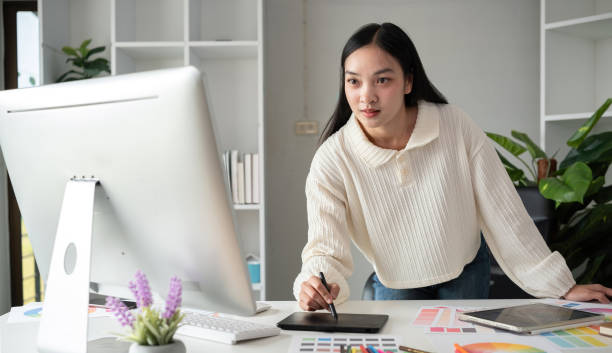 istock Female designer working in graphic design Choose colors for graphic design work. Focused work on a table full of colored paper for working on a computer 2151691630