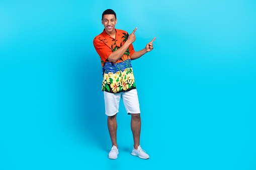 Full length photo of positive cheerful guy dressed print shirt showing two fingers empty space isolated blue color background.