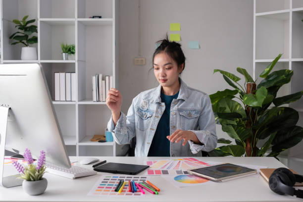 istock Female designer working in graphic design Choose colors for graphic design work. Focused work on a table full of colored paper for working on a computer 2151691722