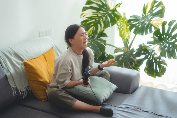 istock Asian woman using joystick playing game feeling upset after lose in game sitting on sofa at home. 2151695612