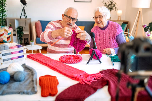 Grandmother showing knitting to her husband sitting in front of camera in living room