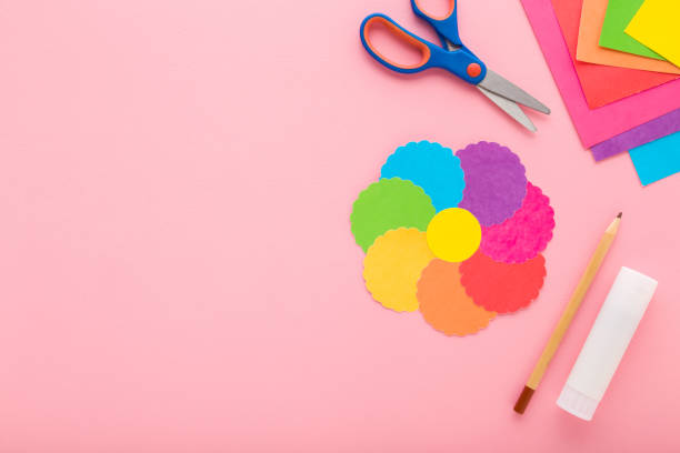 istock Colorful flower shape, scissors, glue stick, pencil and application paper on light pink table background. Pastel color. Closeup. Making decoration elements. Empty place for text. Top down view. 2151696983
