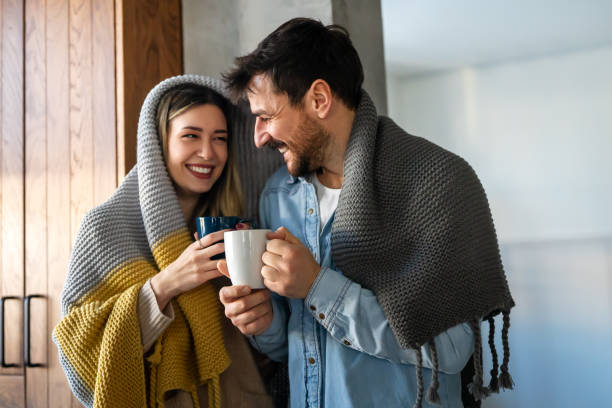 istock Happy young couple with hot drinks cuddling under warm blanket at home 2151697497
