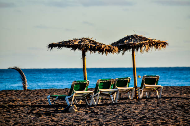 A beach scene with a few umbrellas and chairs. The chairs are arranged in a row and the umbrellas are set up in a line, real image