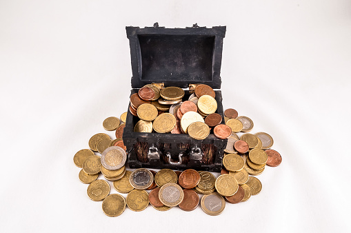A treasure chest full of coins is on a white background. The coins are of different sizes and colors, including gold, silver, and bronze. Concept of wealth and abundance, real image