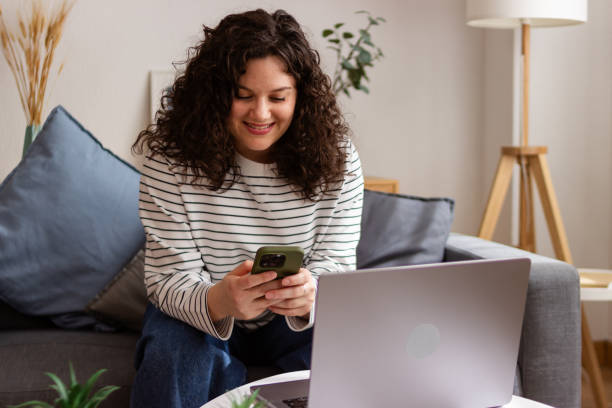 istock Smiling woman using smartphone and laptop at home 2151706730