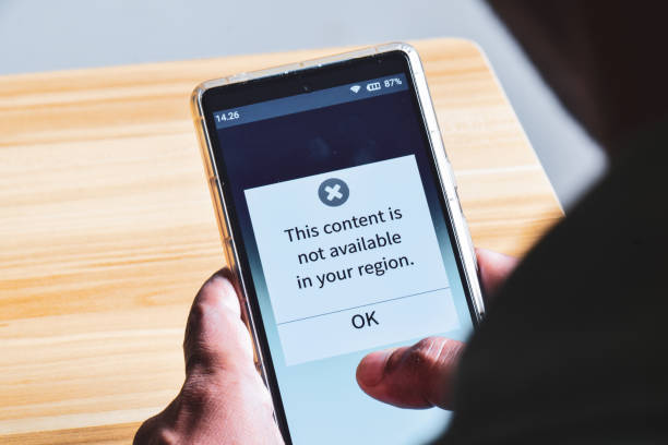 istock Man got notification on his mobile phone that the content is not available in your country. Geo- restrictions or geo- block, access using VPN concept. 2151710048