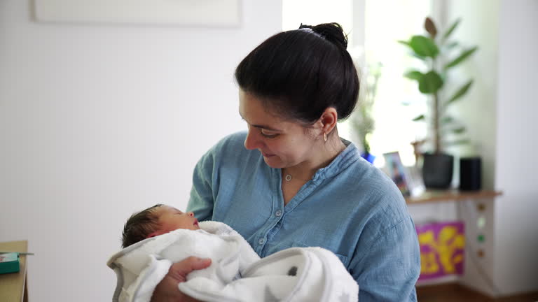 Happy mother holding newborn baby laughing and smiling in carefree expression seated at home living-room. authentic lifestyle scene of maternal care