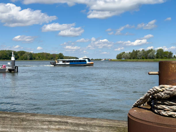 Dordrecht, Netherlands - April 29, 2024: A water bus service on the river Maas to Rotterdam stopping at towns along the journey. Boat departs from the stop in Dordrecht, a spring scenic river scene.