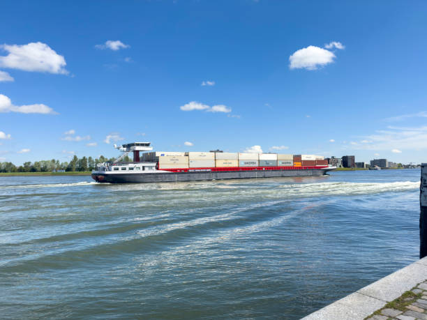 Dordrecht, Netherlands - April 29, 2024: Inland barge freight shipping transport sailing past Dordrecht on the river Maas. Container ship transporting goods in metal containers under Dutch summer sky.