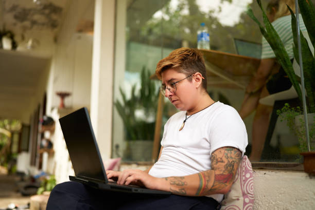 istock Transgender pro works on laptop outdoors, focused on task. Relaxed office environment, gender diverse inclusive scene. Comfortable casual attire, sunny business setting, remote work. 2151721405